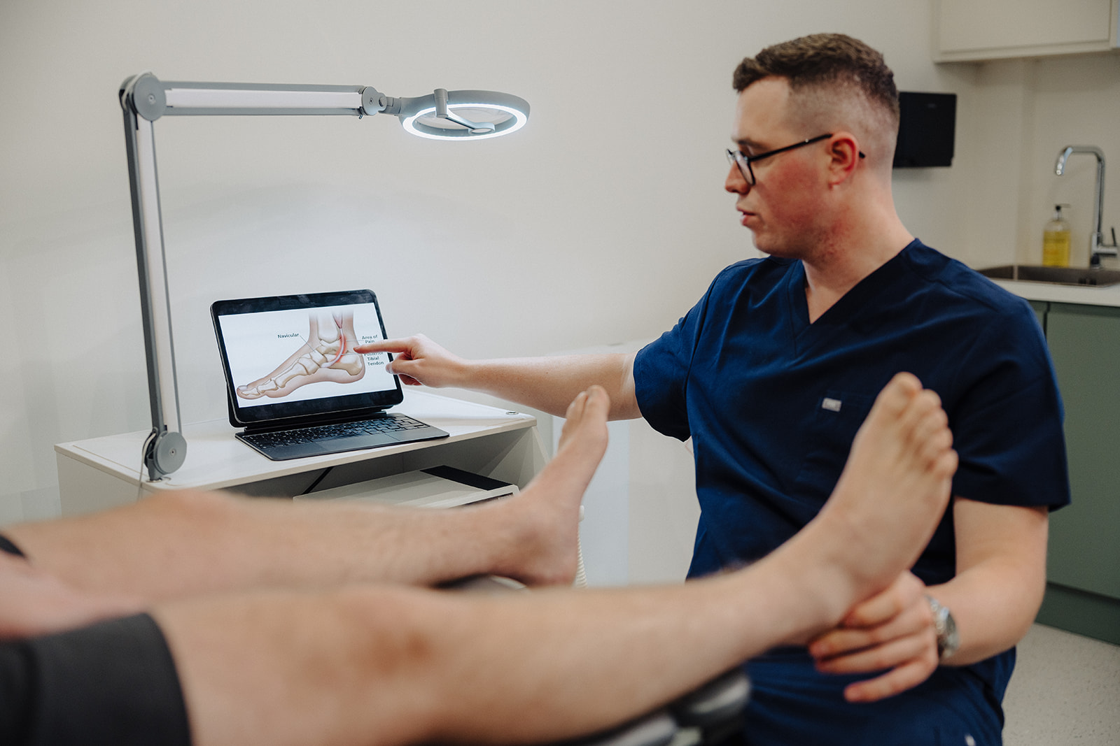 Podiatrist explaining a foot anatomy diagram to a patient during a heel pain assessment at Assure Health in Carryduff, Belfast