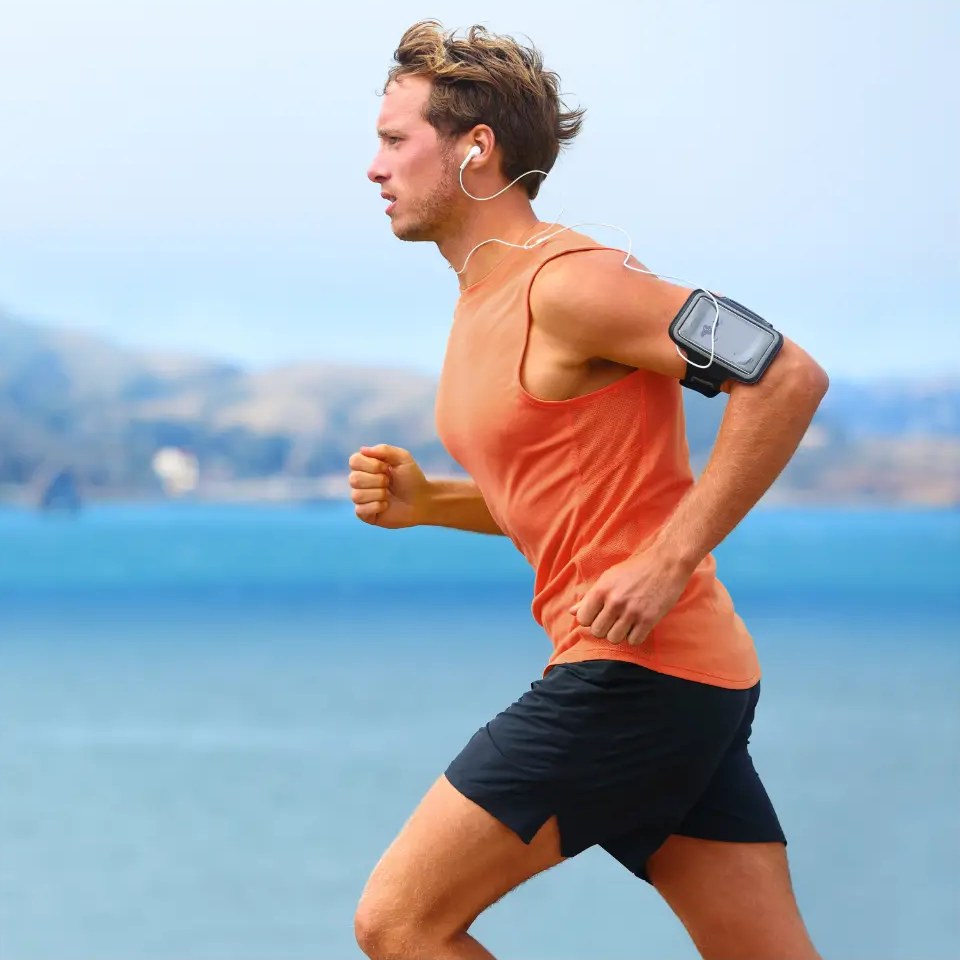Runner in an orange vest running beside the sea, training outdoors near Belfast