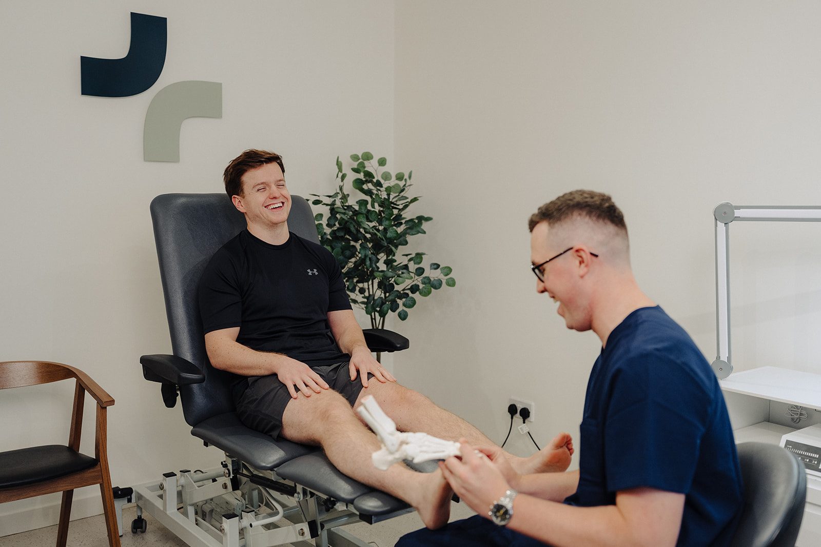 Podiatrist explaining a patient's foot condition using an anatomical foot model at Assure Health, Carryduff